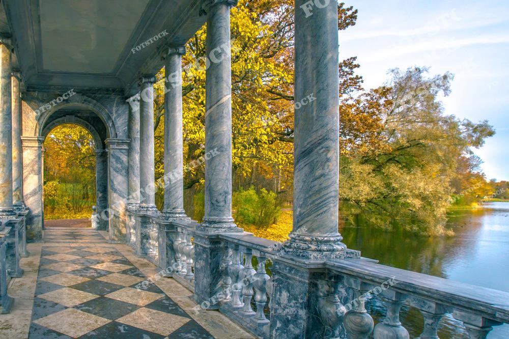 На фотографии изображена Мраморная галерея в Екатерининском парке Царского Села, расположенного в Пушкине, недалеко от Санкт-Петербурга. Архитектурное великолепие галереи с её мраморными колоннами и шахматным полом дополняется осенними красками парка. Это место славится своей красотой и привлекает туристов, особенно осенью, когда природа вокруг галереи превращается в живописное золотое убранство.